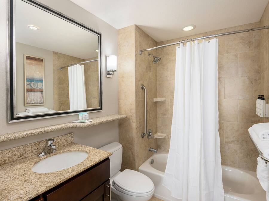 Une salle de bain moderne avec un lavabo sur un plan de travail en granit, des toilettes, une baignoire et une douche dotée d’une porte en verre.