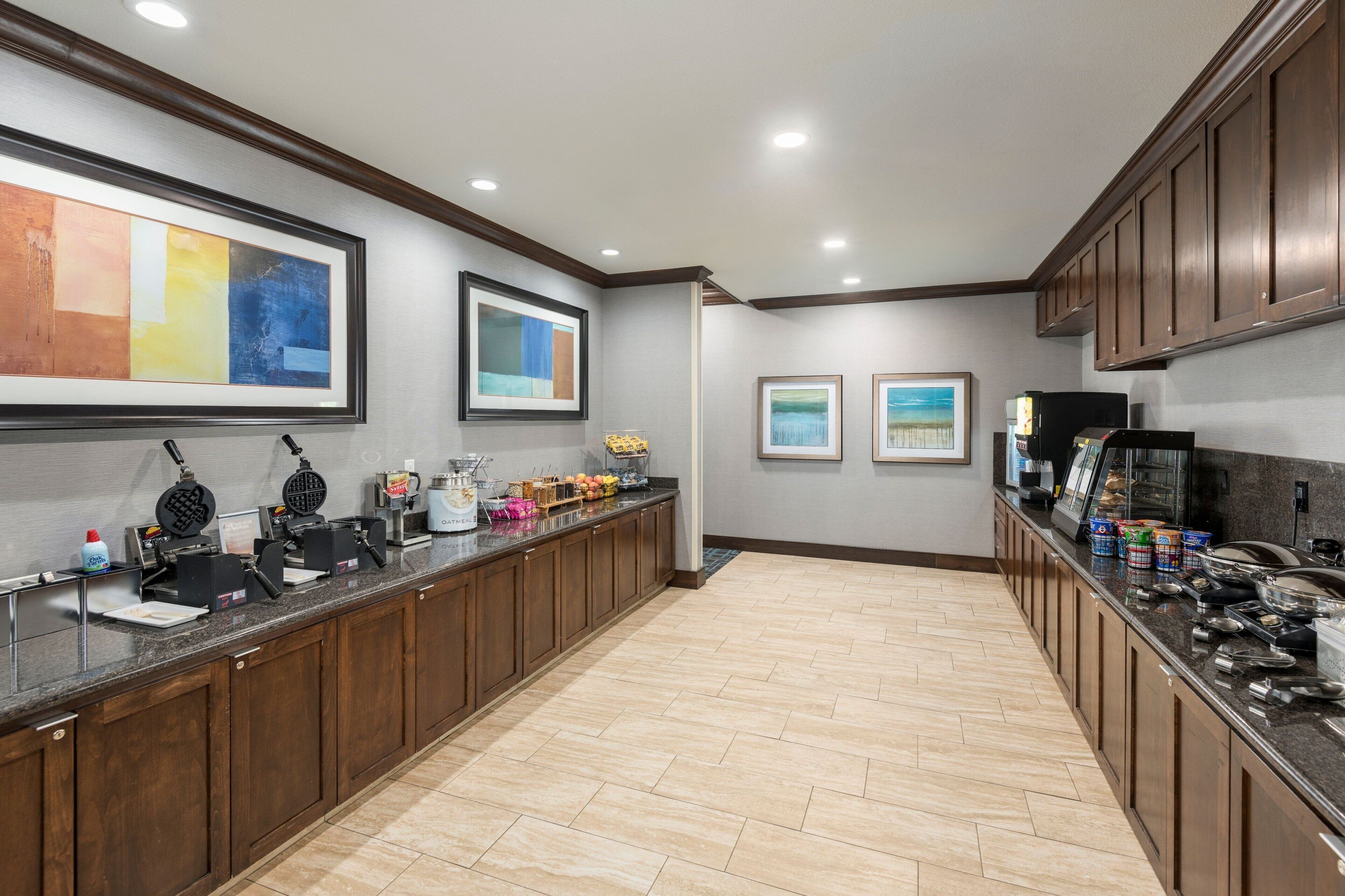 A modern kitchen with a long counter, waffle maker, coffee station, and framed artwork on the walls.