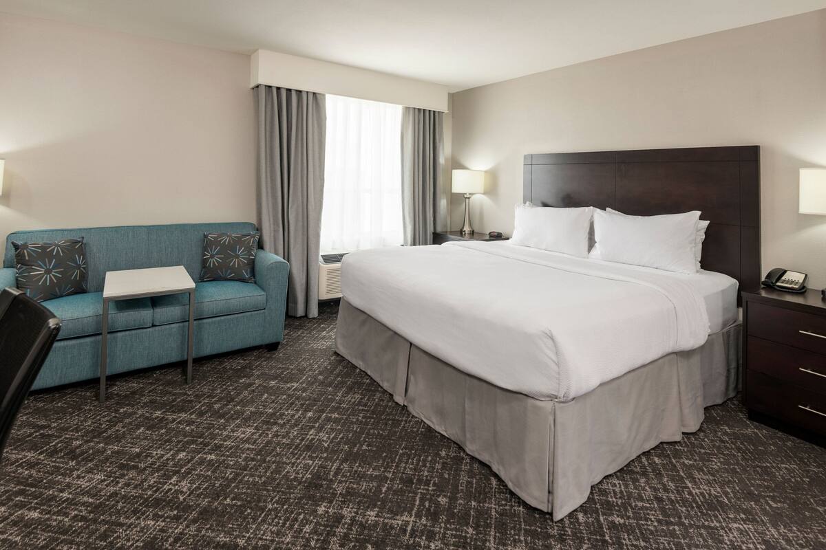 A hotel room with a large bed, a blue sofa, a small table, and a desk with a lamp.