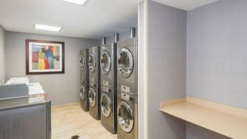 A laundry room with four front-loading washing machines, a drying rack, and a framed abstract painting on the wall.