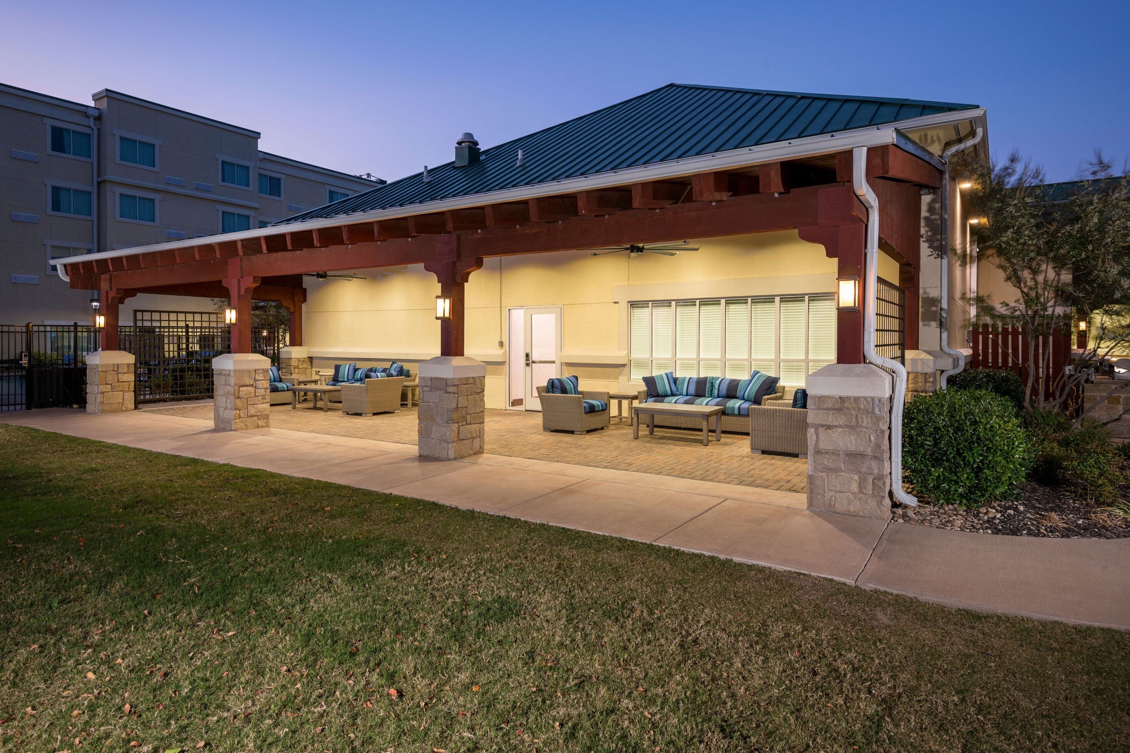 A covered outdoor seating area with stone pillars, a patio, and a building with a blue roof in the background.