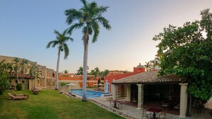 Un área de piscina con sillones reclinables, una fuente y un espacio de descanso cubierto con mesas y sillas.