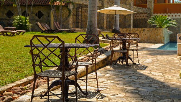 Terraza al aire libre con mesas y sillas, piscina y un sendero de piedra.