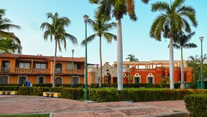Un patio con palmeras, un camino accesible para sillas de ruedas y edificios de arquitectura tradicional.
