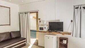 Un espacio habitable compacto con un sofá, un refrigerador pequeño, un microondas, un televisor y un estante de madera con un tostador.