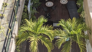 Un patio exterior con cubierta de madera, rodeado de plantas en macetas y una zona de estar con mesa y sillas.