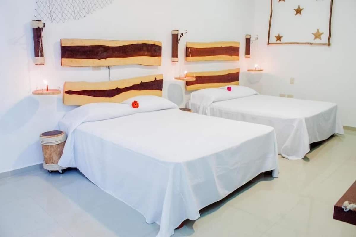 Quarto com duas camas, cada uma com cabeceira de madeira, roupa de cama branca e luminárias laterais.