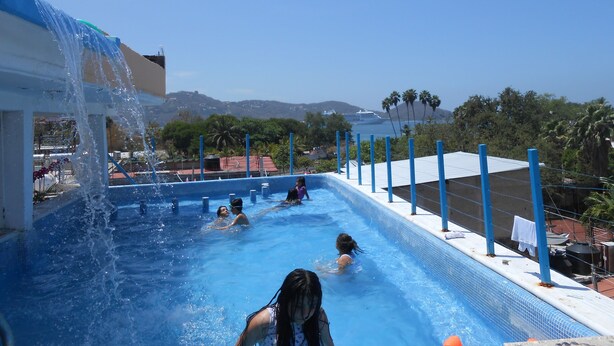 Una piscina con agua azul cristalina, un tobogán y vistas al océano y montañas al fondo.