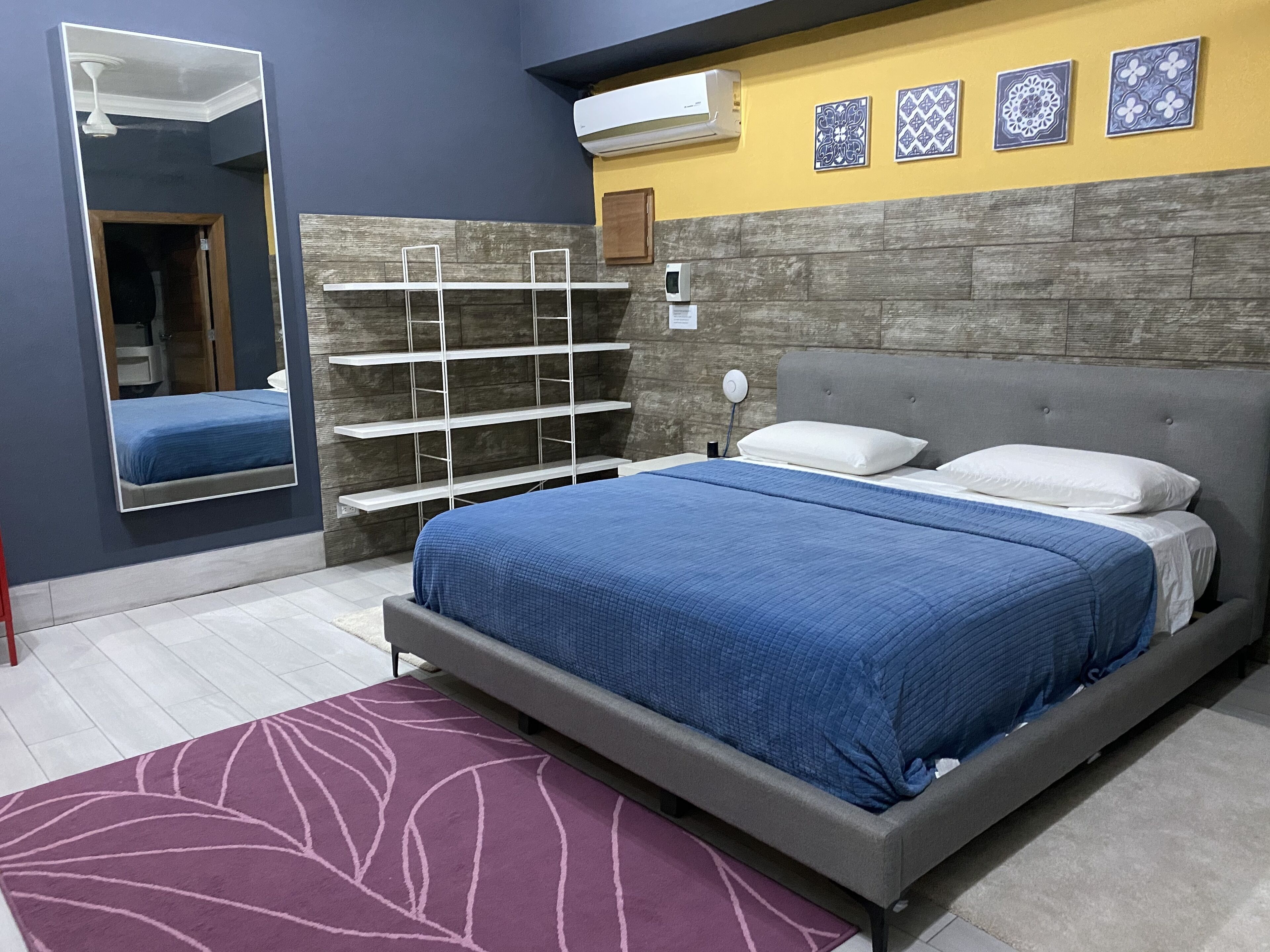 A bedroom with a bed, a mirror, a shelf unit, and decorative wall tiles.