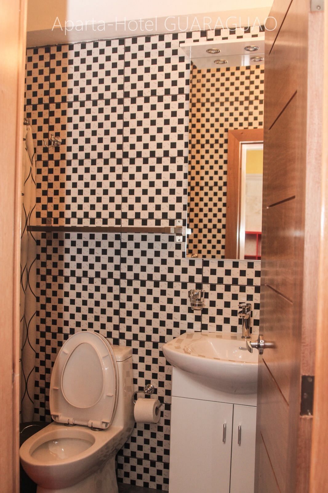 A bathroom with a checkered black and white tile wall, a toilet, a sink, and a mirror.