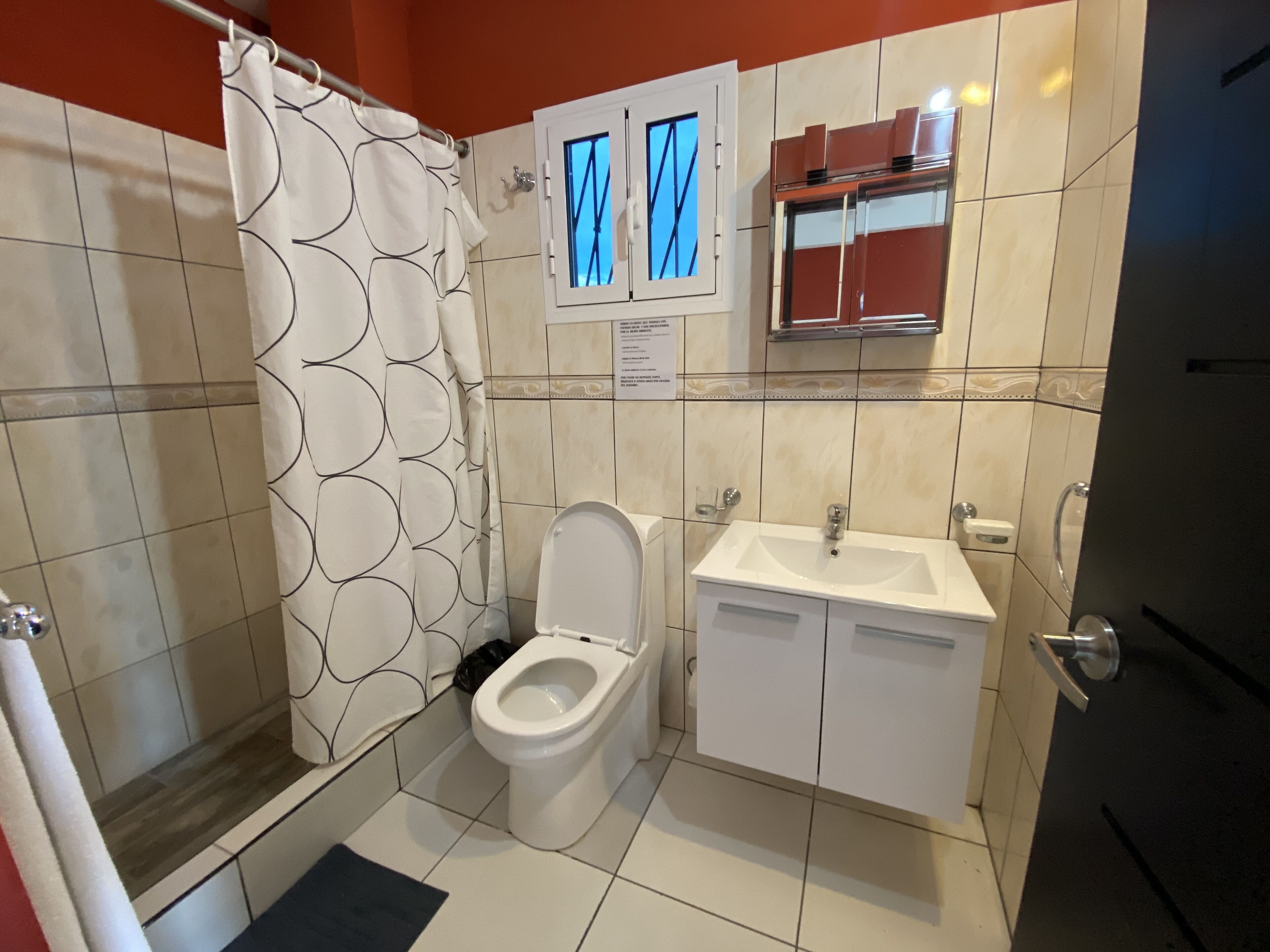 Un baño con inodoro, lavamanos, ducha y ventana con vista al cielo.