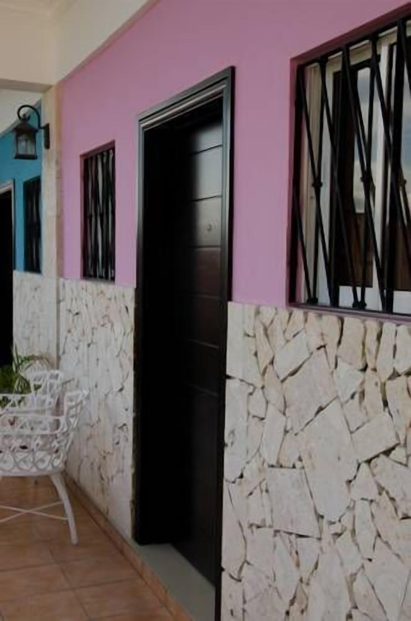 A building with a pink wall, a black door, and a window with a metal grille.