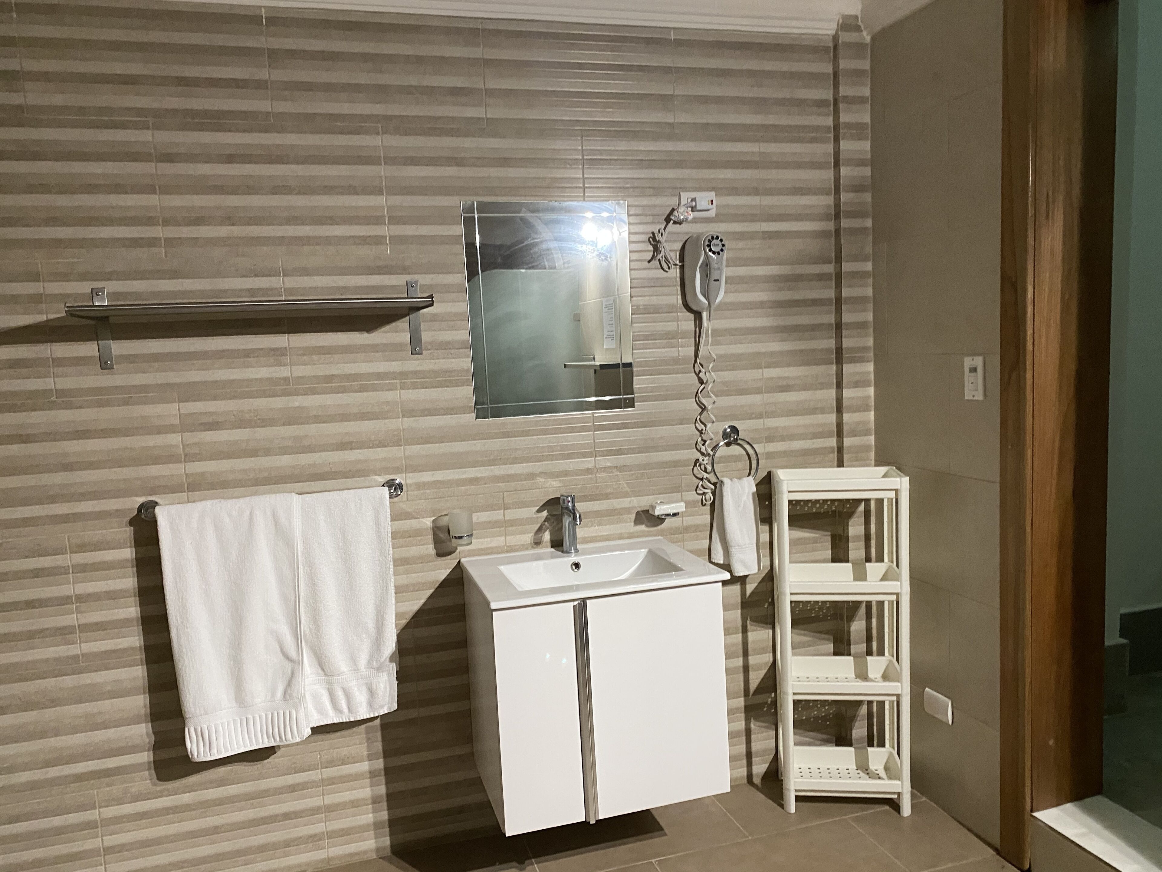 Une salle de bain moderne avec un grand miroir, un lavabo blanc et un porte-serviettes.