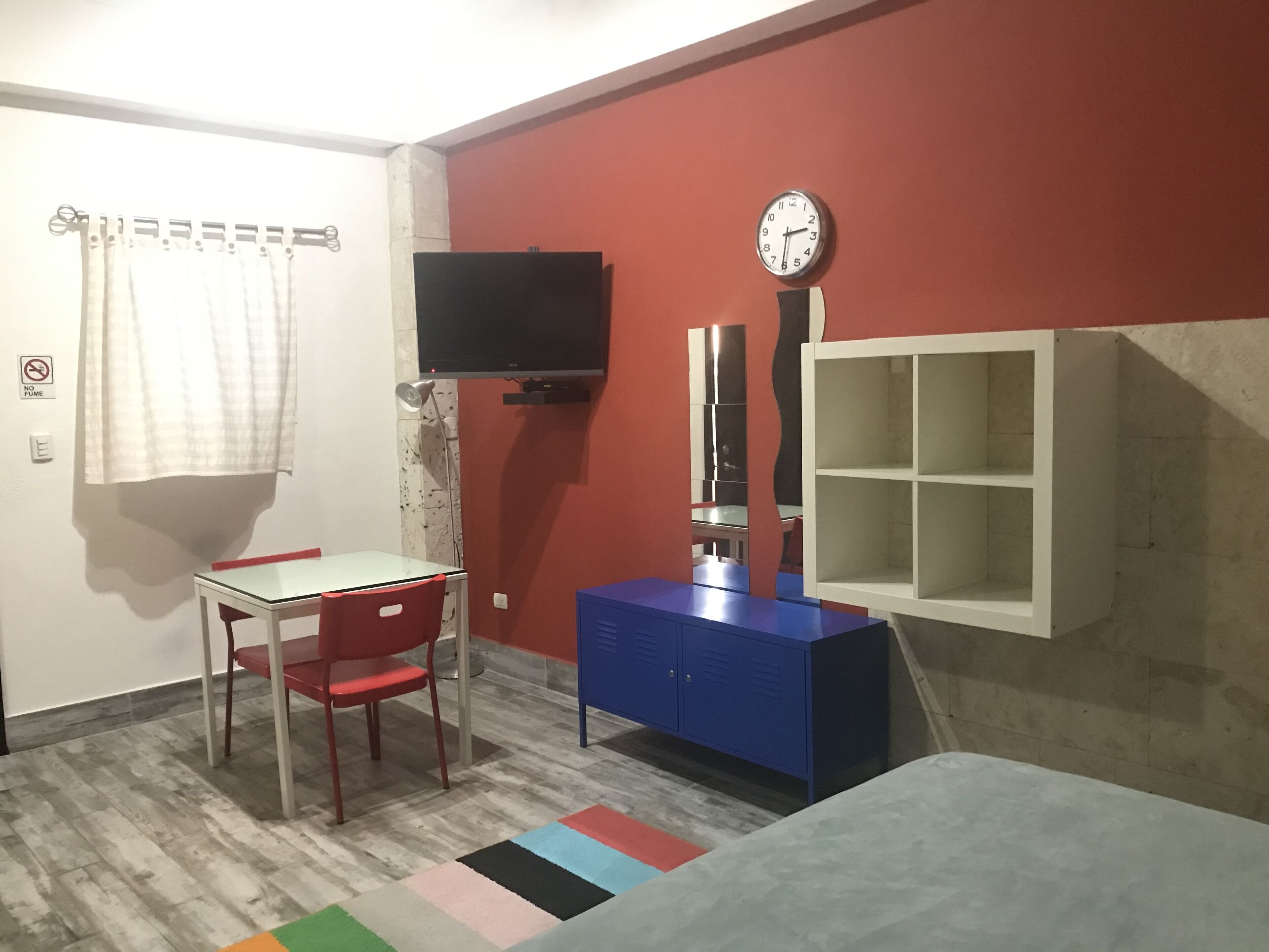 A room with a desk, chair, television, mirror, and storage cabinet.