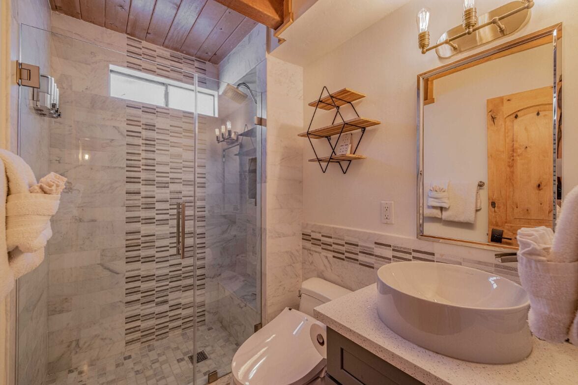 A modern bathroom with a glass-enclosed shower, a large oval sink, and wooden shelves.