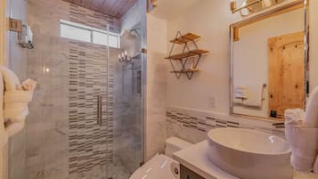 A modern bathroom with a glass-enclosed shower, a large oval sink, and wooden shelves.
