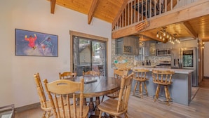 Een ruime eethoek met een houten tafel en stoelen, een keuken met moderne apparatuur, en een groot raam met uitzicht op de omgeving.