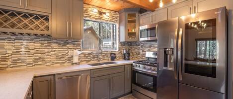 A modern kitchen with stainless steel appliances, a stone backsplash, and wooden ceiling beams.