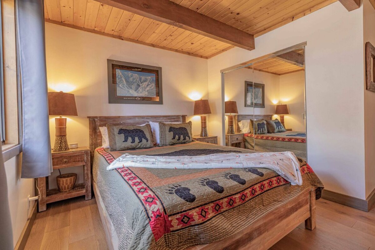 A cozy bedroom with a wooden bed, two bedside lamps, a mirror, and a framed picture on the wall.