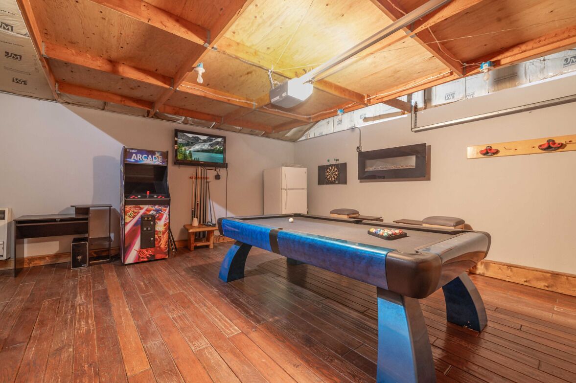 A pool table in a room with wooden flooring and a high ceiling.