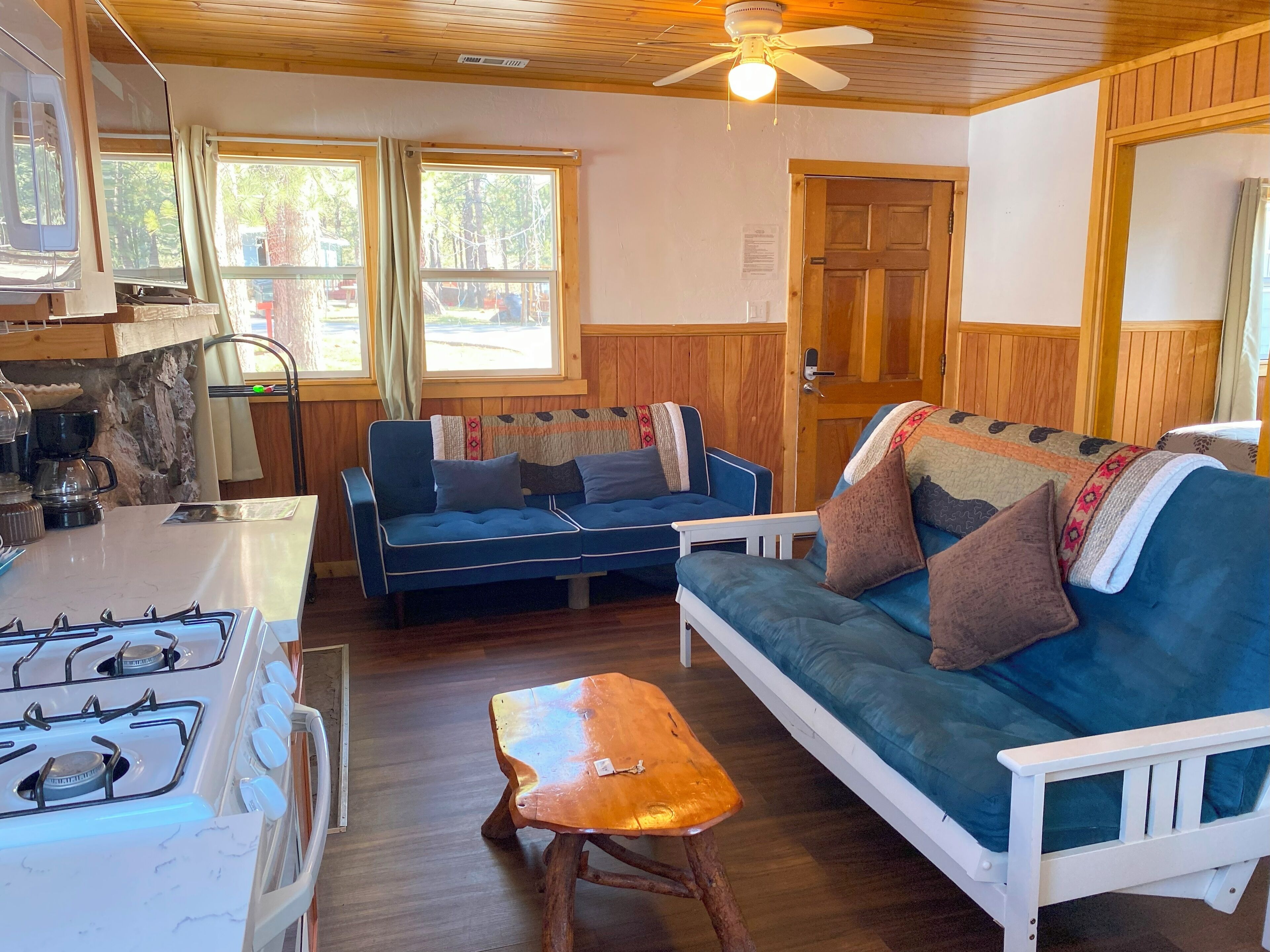 A cozy cabin interior with a kitchen area, a sofa, and a wooden table.