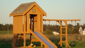 A wooden playhouse with a slide and climbing ladder.