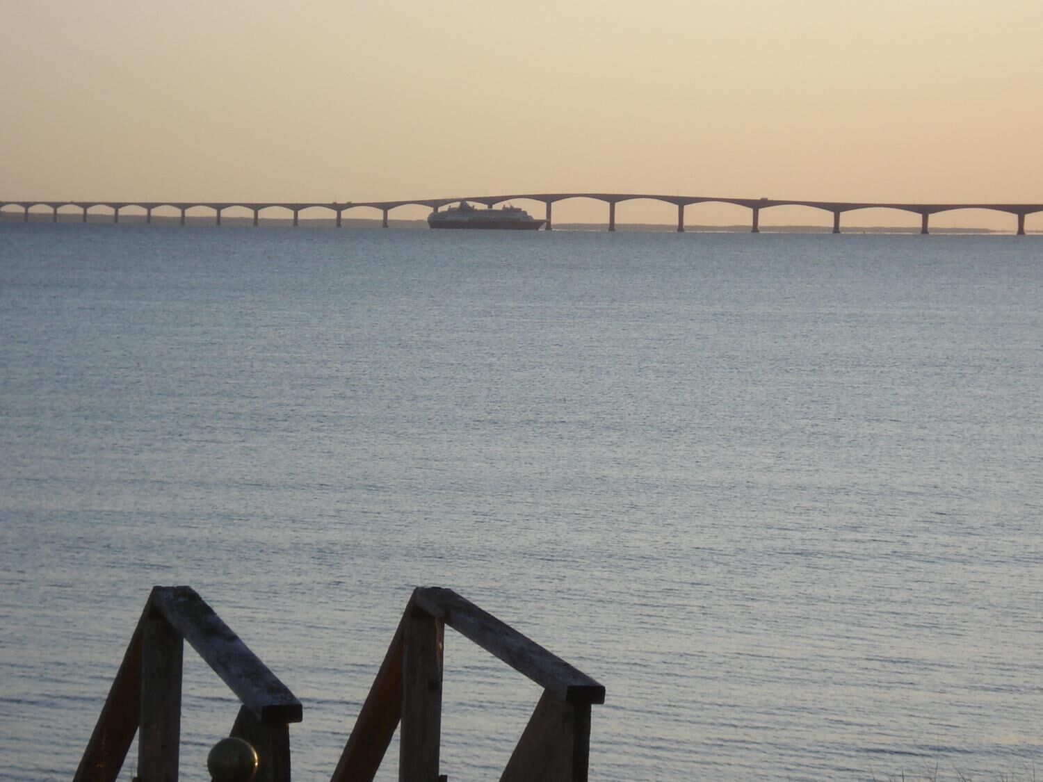 Un pont enjambant une étendue d’eau calme, avec un navire visible au loin.