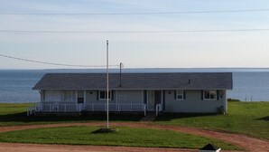 A single-story house with a front porch, a flagpole, and a view of the ocean. - Seabreeze Cottage (Cape Traverse)