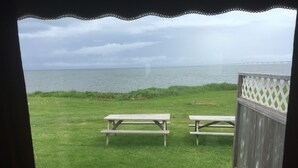 A view from a window overlooking a grassy area with two picnic tables and a wooden fence. - Seabreeze Cottage (Cape Traverse)
