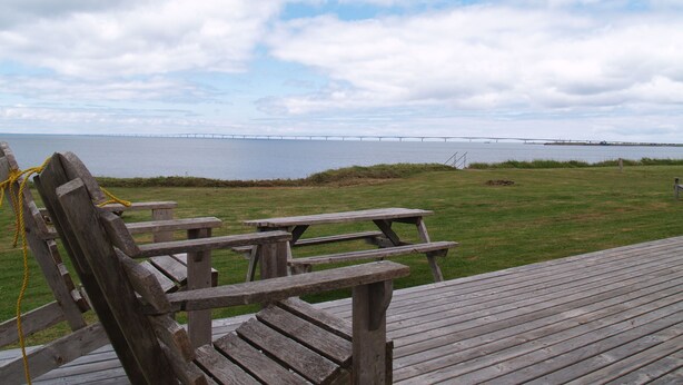 A wooden deck with picnic tables and chairs overlooking a body of water and a bridge. - Seabreeze Cottage (Cape Traverse)