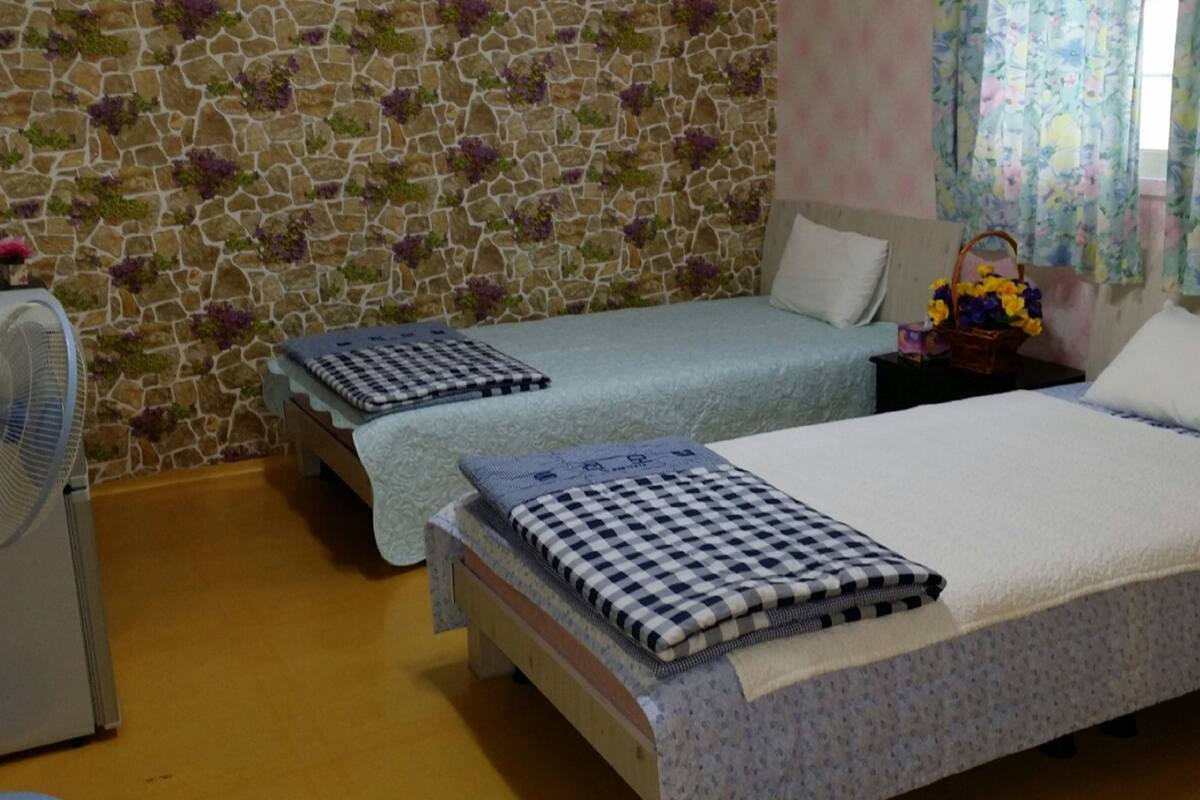 Un dormitori amb dos llits individuals, un ventilador, una paret de pedra i una cortina amb motius florals.
