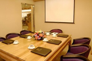 A conference room with a wooden table, purple chairs, a projector screen, and a floral centerpiece. - Kai Du Hotel (Taoyuan City)