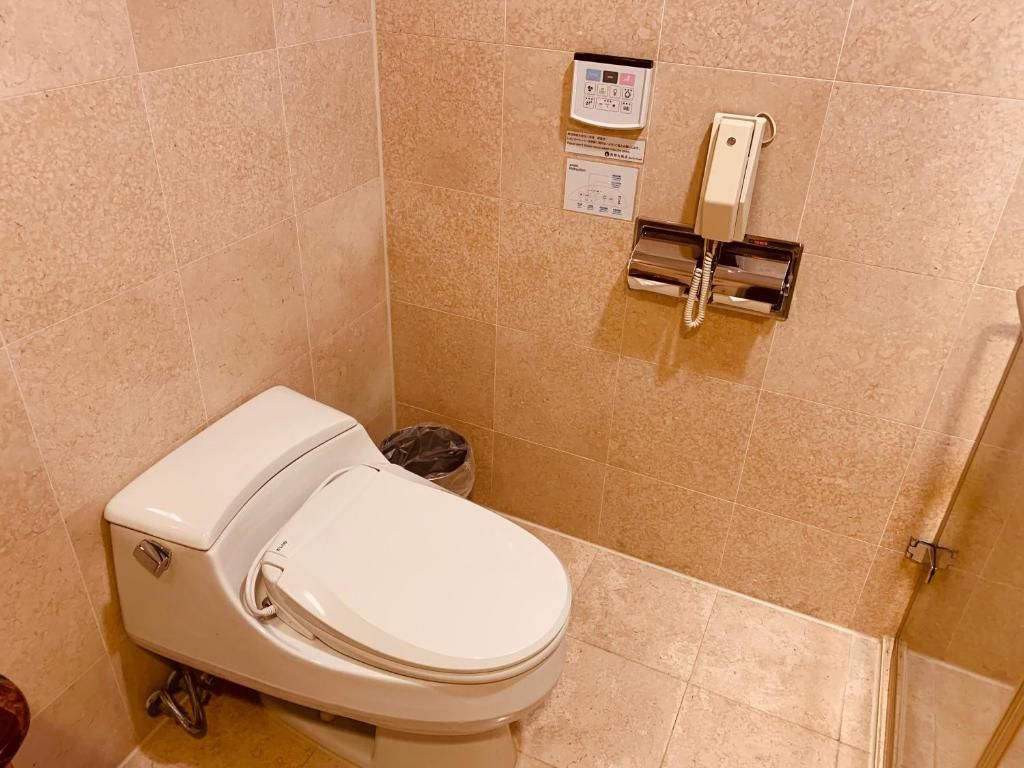 A bathroom with a toilet, a trash bin, and a wall-mounted phone.