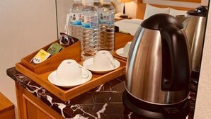 A hotel room with a marble countertop, a tray with water bottles, a kettle, and a bed with a wooden headboard. - Kai Du Hotel (Taoyuan City)