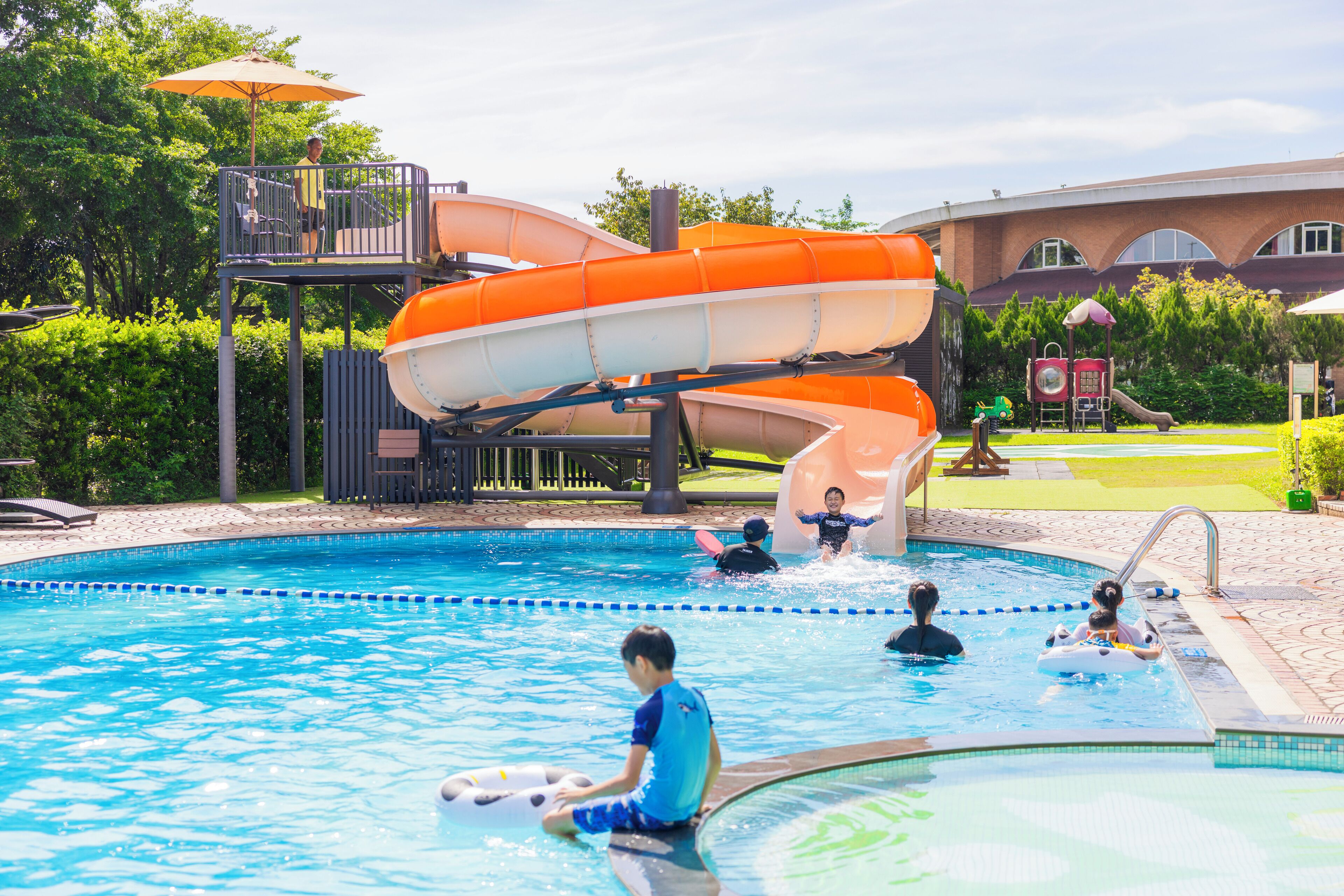 A swimming pool with a water slide, lounge chairs, and a playground area.