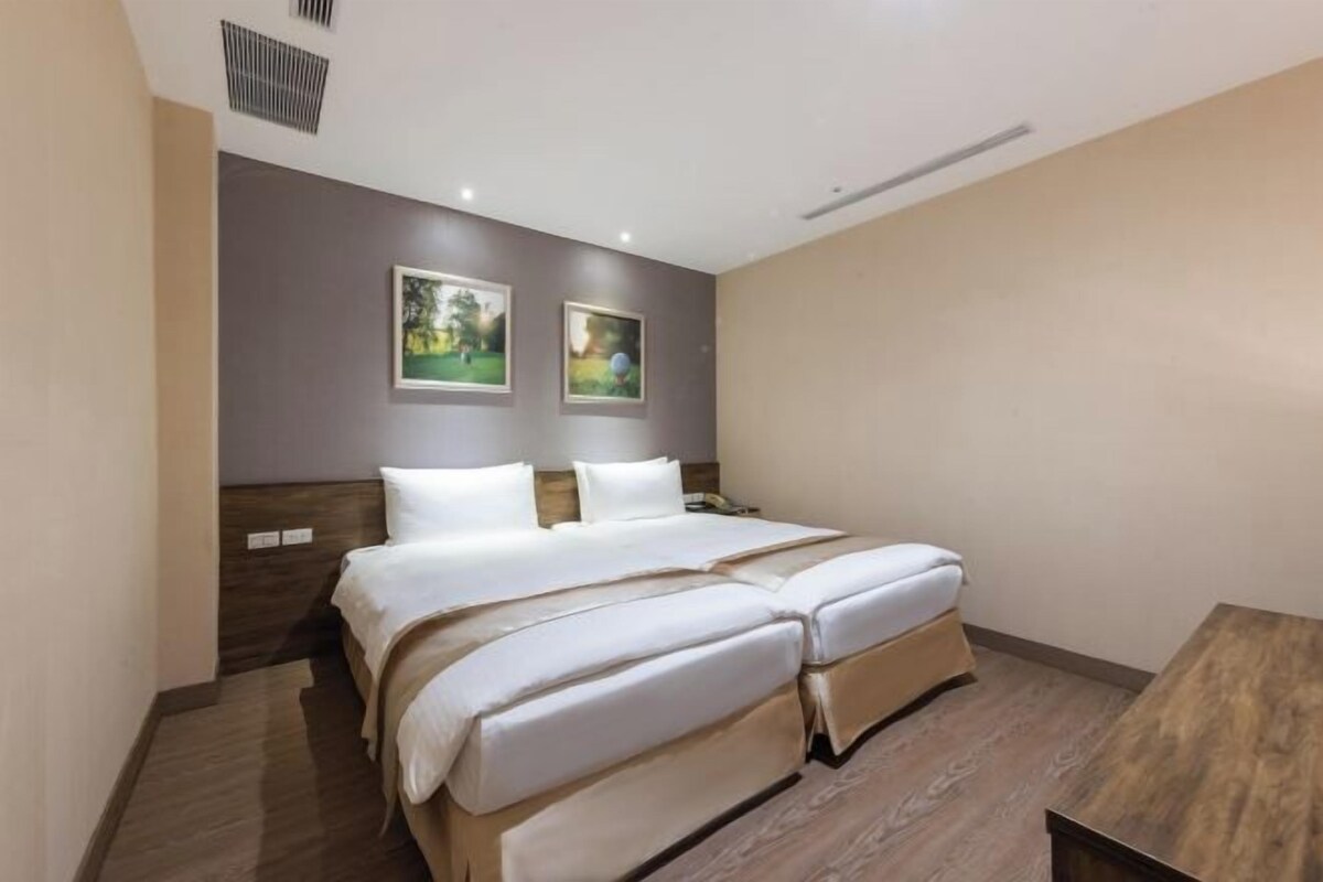 A hotel room with a double bed, a wooden headboard, two framed pictures on the wall, and a small table.