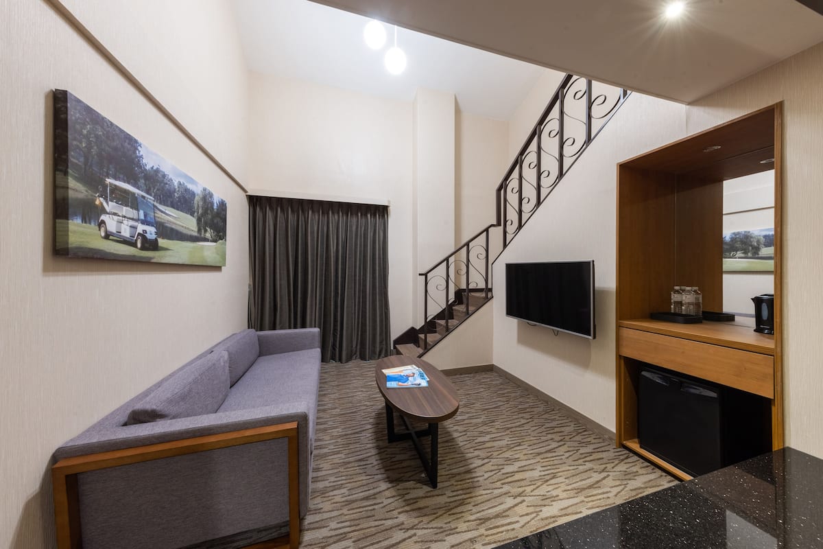 A modern living room with a grey sofa, a small table, a staircase, a flat-screen TV, and a kitchen area with a coffee maker.