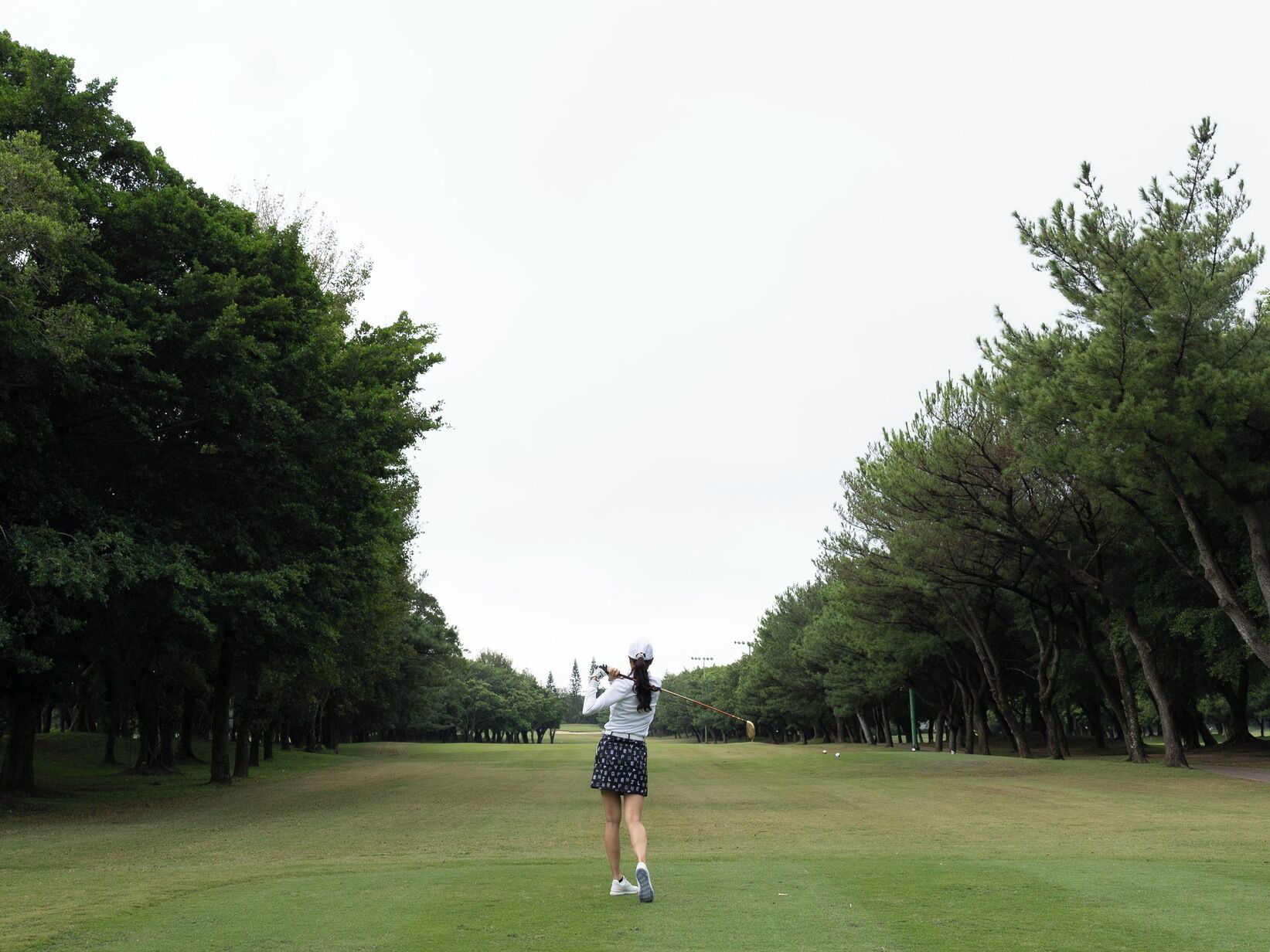 A person playing golf on a course surrounded by trees.