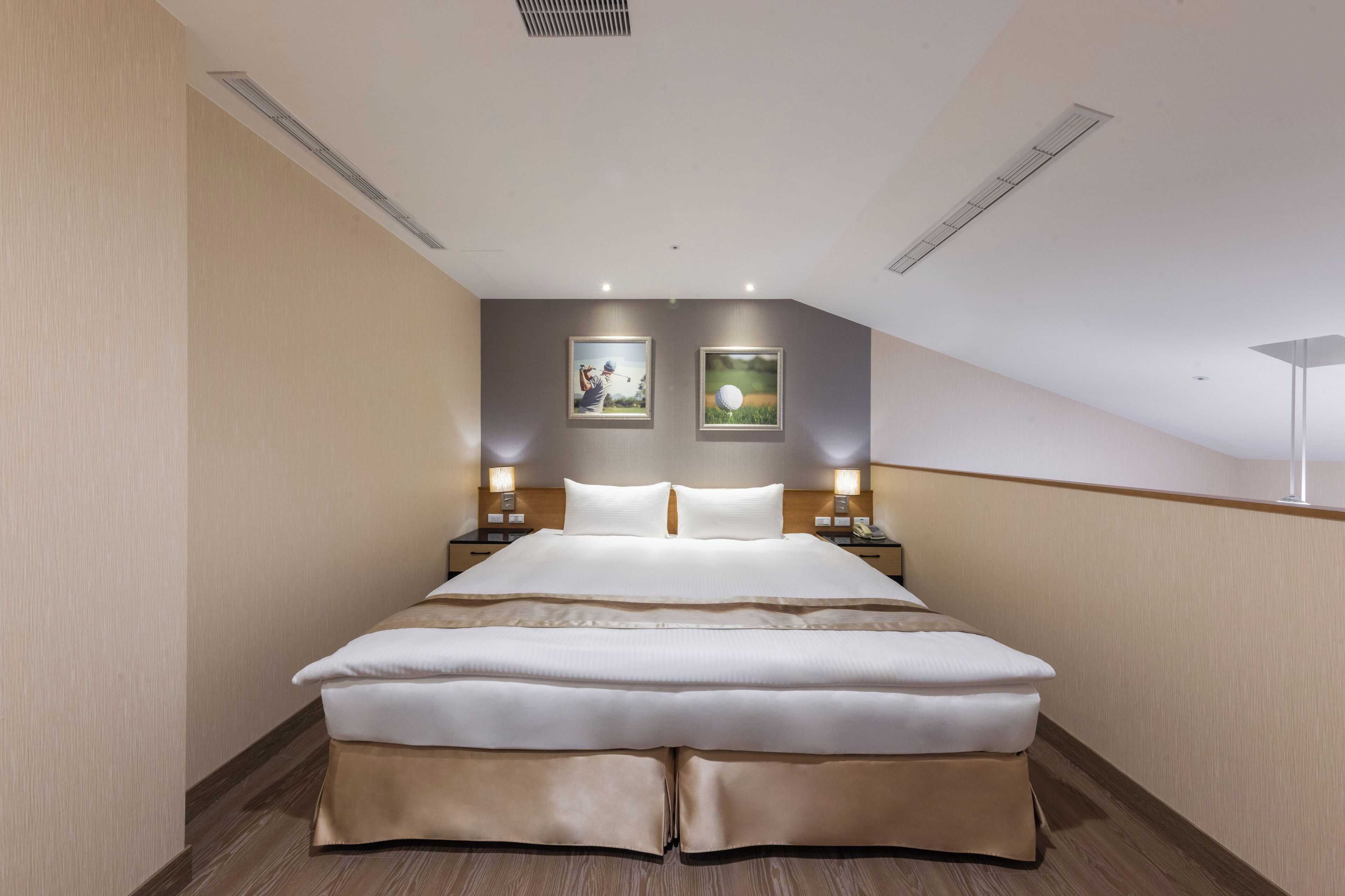 A modern hotel room with a large bed, two bedside tables with lamps, and two framed pictures on the wall.
