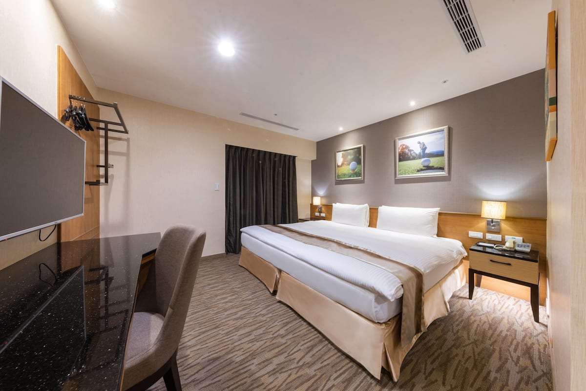 A hotel room with a bed, a desk, a chair, a TV, and artwork on the walls.