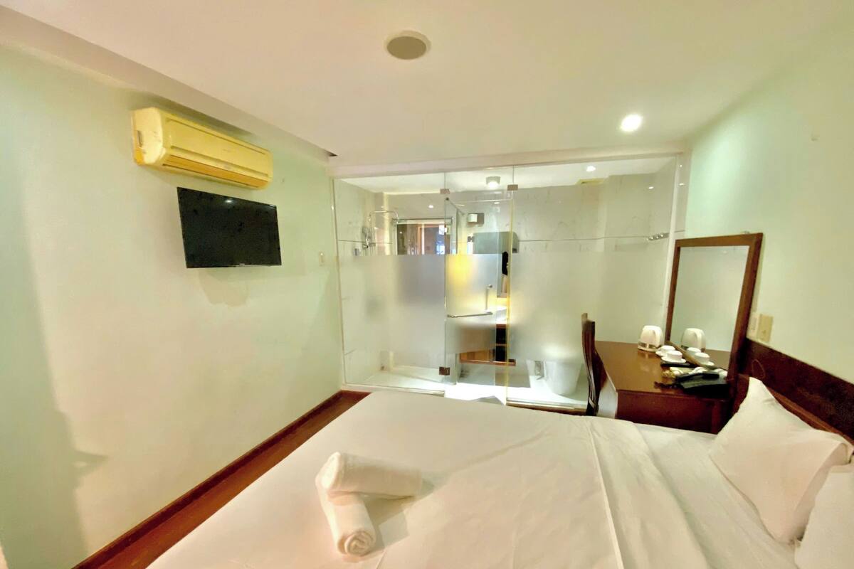 A hotel room with a bed, a bedside table with a lamp, a mirror, and a wall-mounted TV.