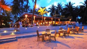 Un restaurante frente a la playa con terraza y palmeras.