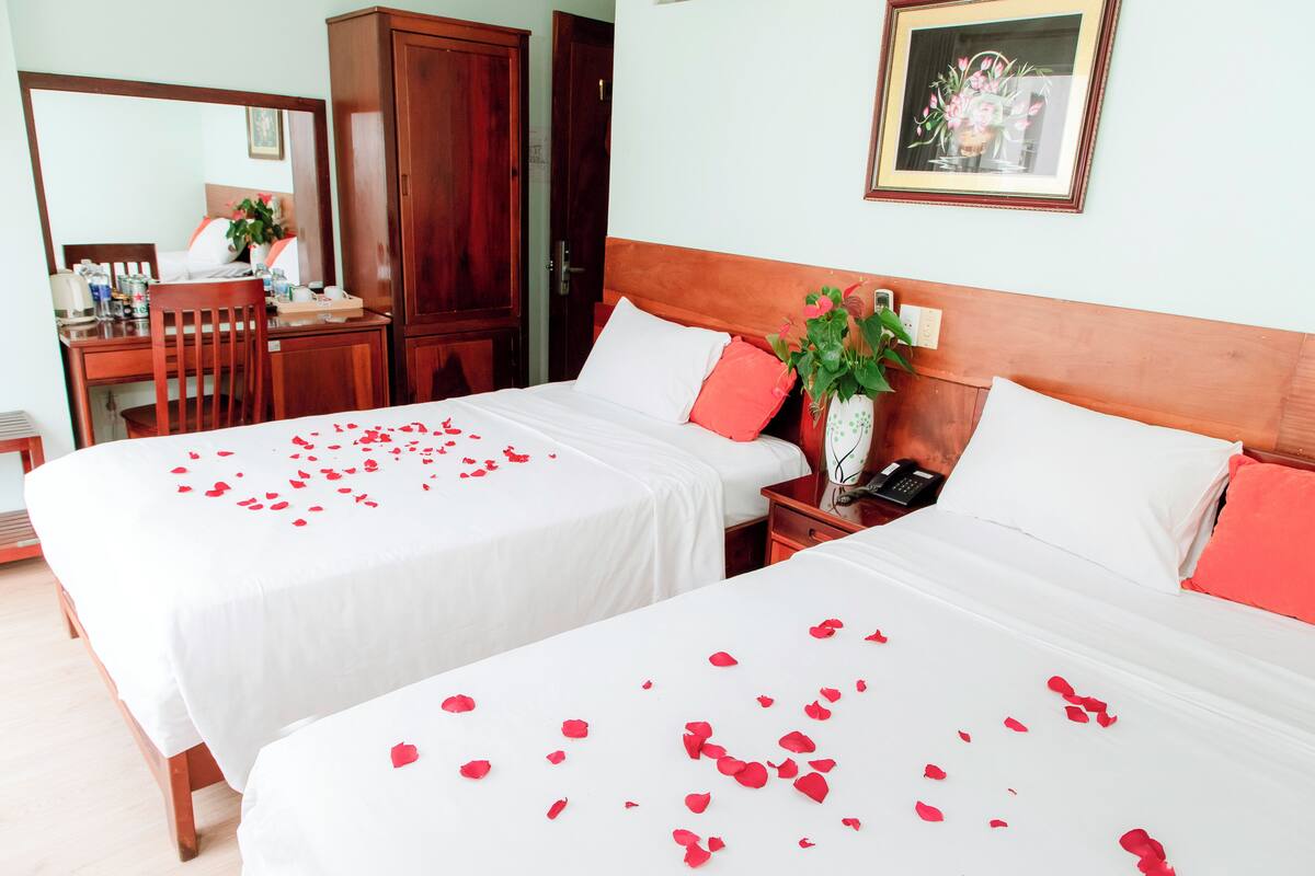 A hotel room with two beds, a wooden wardrobe, a desk with a chair, and a mirror.