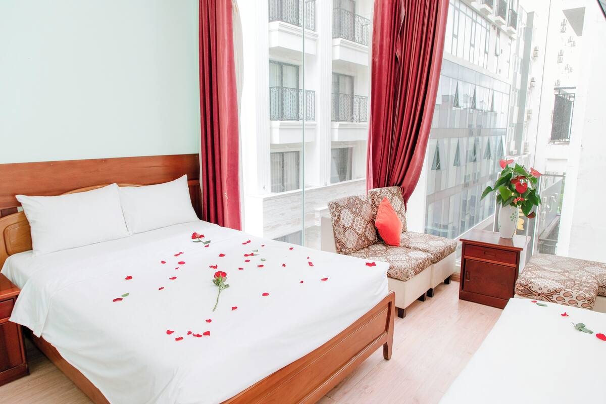 A hotel room with a bed, a chair, a nightstand, and a window with curtains.