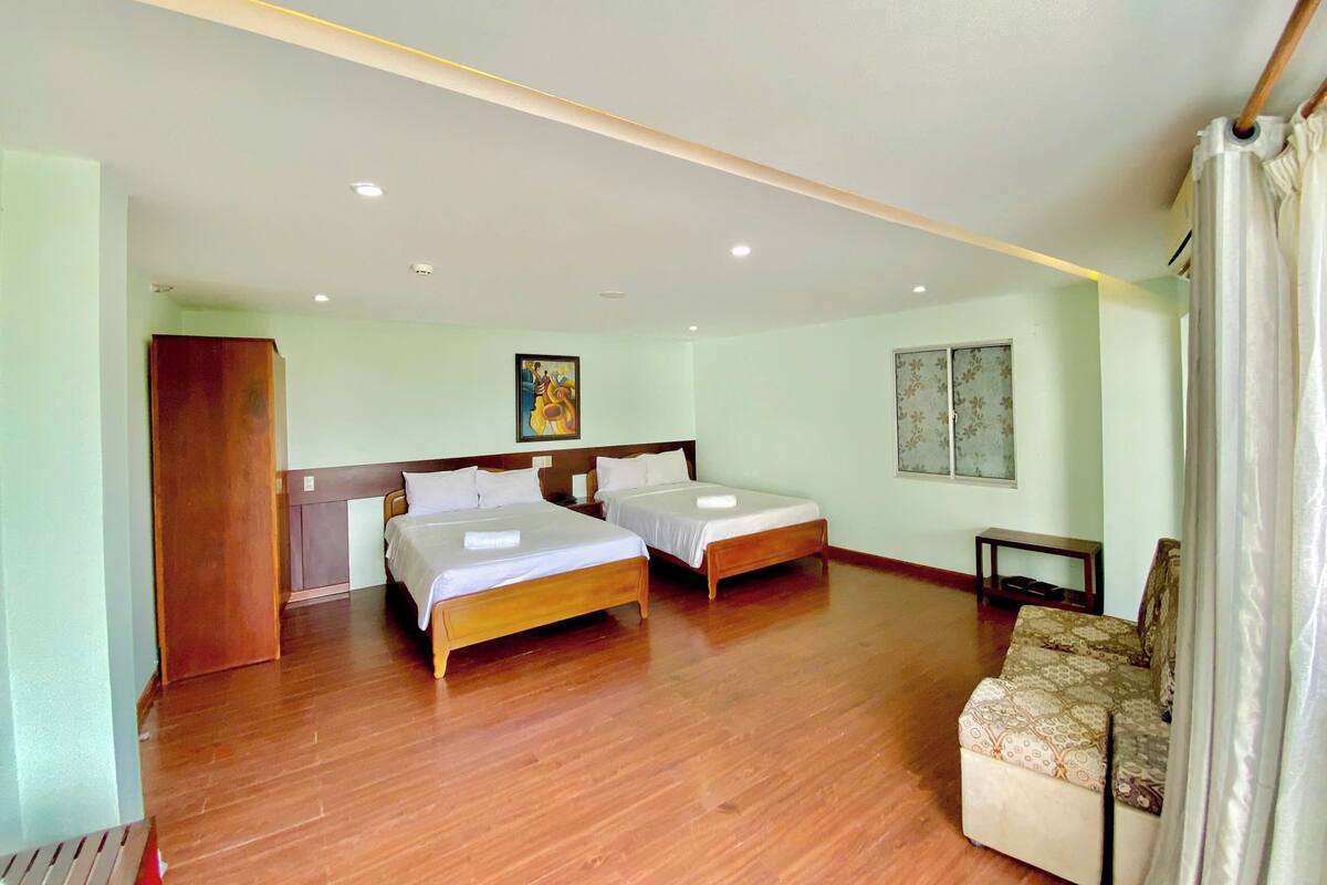 A hotel room with two wooden beds, a sofa, a painting on the wall, and a window with curtains.