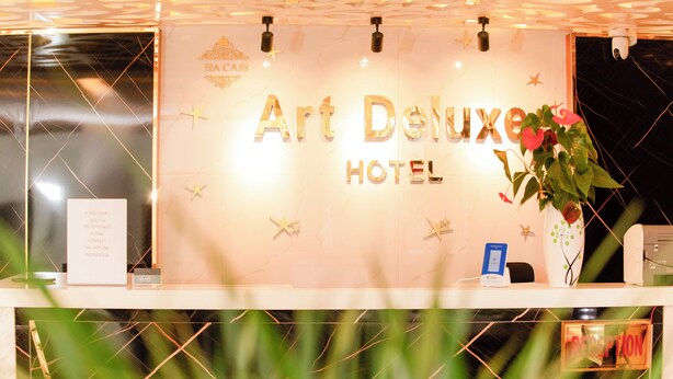 Mostrador de recepción en el Hotel Art Deluxe, con un cartel, una planta y una barra de recepción.
