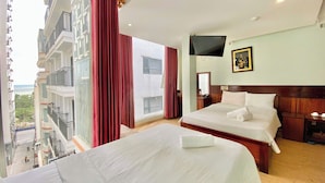 Habitación de hotel con dos camas, televisión, escritorio y un amplio ventanal con cortinas.