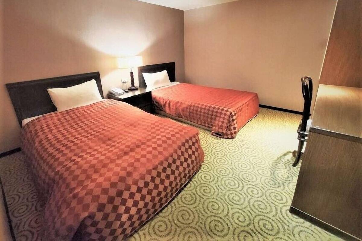 Une chambre d’hôtel avec deux lits, une table de chevet, une lampe et un réfrigérateur.