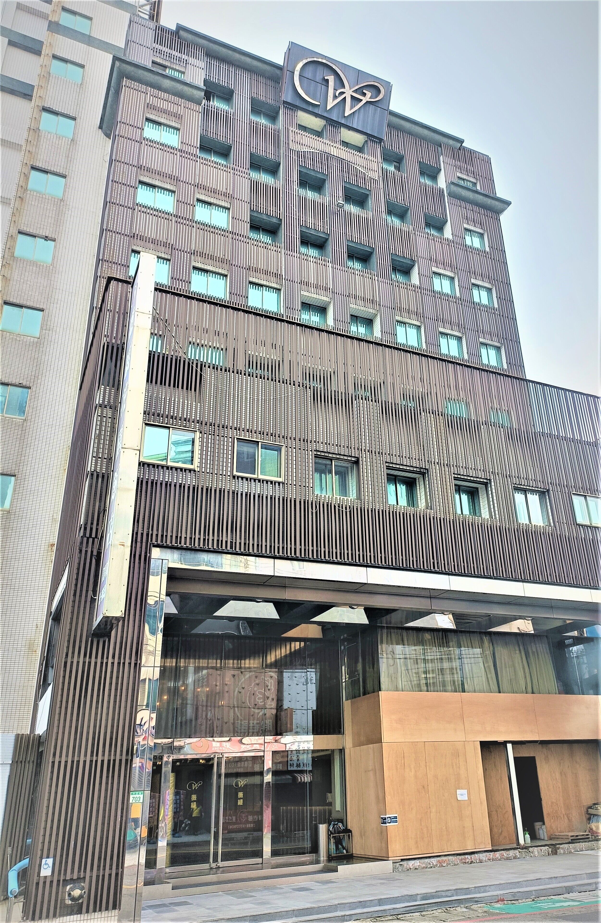 A multi-story hotel with a modern design, featuring a prominent logo at the top.