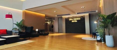 Un lobby de hotel moderno con suelo de madera, sofás negros, una lámpara de pie roja y una recepción.